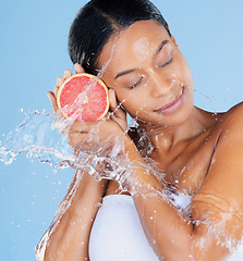 Image showing Black woman, water splash or skincare grapefruit on blue background in facial hydration, healthcare or isolated wellness. Beauty model, happy or wet with citrus food for vitamin c or face dermatology