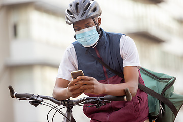 Image showing Courier service, delivery and black man with phone, shipping app with face mask for Covid compliance. Eco friendly travel, outdoor and communication with ecommerce and bike, retail and distribution