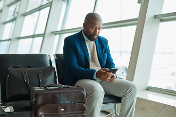 Image showing Black man, phone and luggage at airport for business travel, trip or communication waiting for flight. African American male traveler chatting or checking plain times, schedule or delay on smartphone