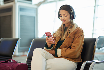 Image showing Music headphones, phone and woman at airport lobby on social media, internet browsing or web scrolling. Travel, mobile technology and female with smartphone app for streaming radio, podcast or song.