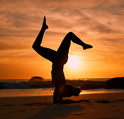 Image showing Yoga, silhouette or handstand on sunset beach, ocean or sea in evening workout or relax exercise training. Yogi, woman or sand balance pose at sunrise for healthcare wellness fitness or strong body