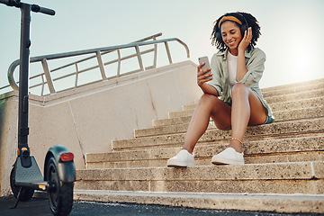 Image showing Black woman outdoor, scooter and phone with headphones for music, eco friendly travel and 5g for audio streaming in city. Sustainability, listen to podcast and relax on steps with transportation