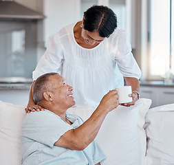 Image showing Mature couple, bonding or giving coffee on sofa in house, home or relax living room in support, love or trust help. Smile, happy or retirement woman with morning tea cup for elderly man in marriage