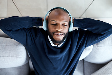 Image showing Top view, music headphones and black man on sofa in home living room streaming audio. Meditation, relax technology and male on couch in lounge listening to peaceful podcast, radio or sound in house.