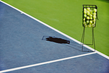 Image showing Tennis, sport balls and basket of sports equipment on a training court outdoor with no people. Exercise, fitness and workout equipment shadow for match of game competition on turf ground in summer