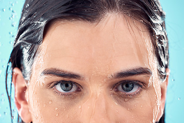 Image showing Water splash, skincare and eyes of woman in shower in studio isolated on a blue background. Beauty, face portrait and young female model washing, cleaning or bathing for hygiene, wellness and health.