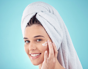 Image showing Face, towel and woman with skincare cream in studio isolated on a blue background. Portrait, dermatology and happy female model apply lotion cosmetics, creme or facial moisturizer for healthy skin.