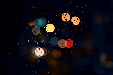 Image showing Night, bokeh and lights on a window with water drops, liquid or moisture against a dark abstract background. Blurred light, colorful and rain drop or splash on glass for city view during rainy season