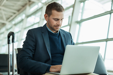 Image showing Business man, airport and laptop for travel while working in lobby to check flight booking. Entrepreneur person with luggage in building while typing or writing email or report on trading investment