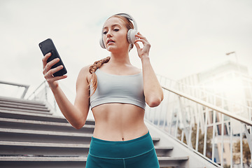 Image showing Woman, runner and phone with headphones for music, radio and web texting on chat app by stairs. Gen z girl, urban workout and fitness with smartphone for networking, social media and internet in city