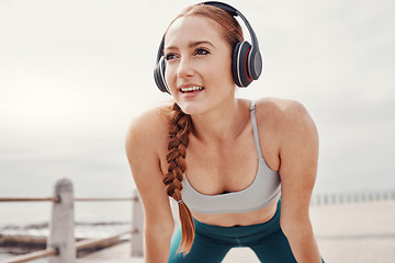 Image showing Running, music and face of woman by ocean with motivation, smile and ready for cardio workout. Fitness, sports and happy girl with headphones in Cape Town for exercise, wellness and marathon training