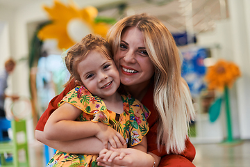 Image showing A cute little girl kissing and hugs her mother in preschool