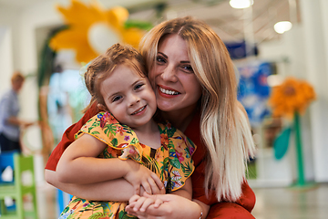 Image showing A cute little girl kissing and hugs her mother in preschool