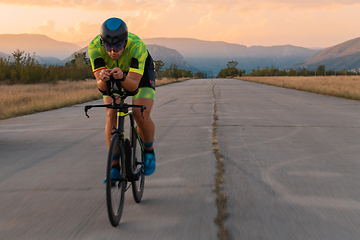 Image showing Triathlete riding his bicycle during sunset, preparing for a marathon. The warm colors of the sky provide a beautiful backdrop for his determined and focused effort.