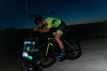 Image showing A videographer recording a triathlete riding his bike preparing for an upcoming marathon.Athlete's physical endurance and the dedication required to succeed in the sport.