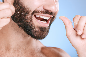 Image showing Dental, floss and oral hygiene with a man in studio on a blue background cleaning his teeth for healthy gums. Dentist, healthcare and mouth with a young male flossing to remove plague or gingivitis