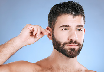 Image showing Ear, cleaning and man with cotton bud in studio for hygiene, grooming and beauty routine on blue background. Earwax, product and guy model in cosmetic, luxury and wax, removal or stick while isolated