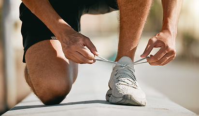 Image showing Fitness, shoes and laces with a man runner getting ready for a cardio or endurance workout closeup outdoor. Exercise, running and workout with a male athlete fastening shoelaces while training