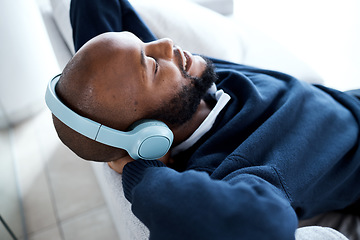 Image showing Music headphones, top view and black man on sofa in home living room streaming audio album. Relax, technology and happy male on couch in lounge listening to fun podcast, radio or sound in house.