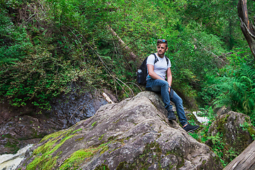 Image showing Man traveler with backpack sitting on rock in the forest.