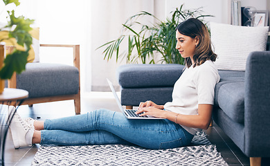 Image showing Woman, laptop and typing sitting on floor in the living room by sofa in remote work or studying at home. Female freelancer working on computer checking email, research or browsing in lounge by couch