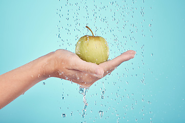 Image showing Water splash, cleaning and hands with apple in studio isolated on a blue background. Nutritionist, fruits and model or woman washing food for healthy diet, vitamin c or skincare, beauty or wellness.