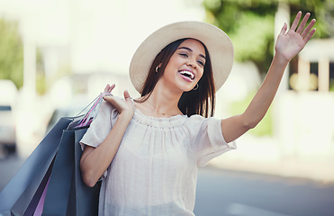 Image showing Woman, shopping bags and hand signal in the city waiting on the street for transport, lift or travel. Happy female shopper waving hands carrying gifts in discount, deal or sale for traveling in town