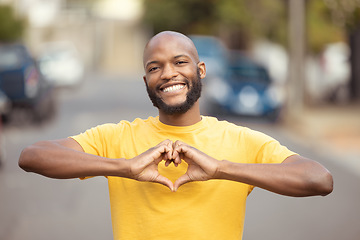 Image showing Portrait, man and hand, heart and love in a city, happy and smile against blurred background space. Emoji, hands and face of male relax with finger, frame and loving message, gesture and travel sign