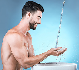 Image showing Water splash, skincare and man cleaning hands in studio isolated on blue background for wellness, healthy skin or hydration. Hygiene, dermatology or smile of happy male model bathing or washing hand.