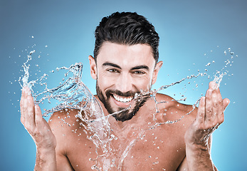 Image showing Portrait, water splash and a man model washing his face in studio on a blue background for hygiene or hydration. Bathroom, skincare and cleaning with a handsome male splashing his skin for beauty