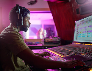 Image showing Black man, studio recording and music job in night with headphones, computer or focus by mixing console. Sound engineer, producer or audio technology for professional production of hit song for radio