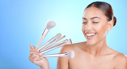 Image showing Woman, brushes and smile for makeup, cosmetics or beauty against a blue studio background. Female gen z model smiling for cosmetic skincare, facial glow aesthetic or foundation product on mockup