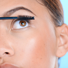 Image showing Makeup, mascara and eyelashes with a black woman in studio on a blue background for beauty. Eyes, cosmetics and zoom with an attractive young female model closeup to apply a cosmetic product