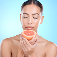 Image showing Skincare, woman and grapefruit scent for in studio for beauty, smell and cosmetics on blue background. Fruit, citrus and product for girl skin model relax in luxury, pamper or routine while isolated