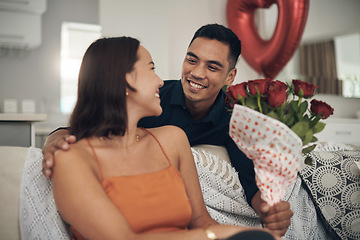 Image showing Valentines day, flowers and couple on a living room sofa with a present and a smile. Happy, love and care of young people together with celebration rose on a date in a house on a couch with a gift