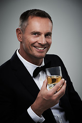 Image showing Tuxedo, whiskey glass and man portrait with alcohol in a suit feeling classy with a luxury drink. Gray background, isolated and studio with a model, agent or actor smile with rich drinking