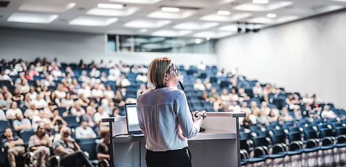 Image showing Female speaker giving a talk on corporate business conference. Unrecognizable people in audience at conference hall. Business and Entrepreneurship event.