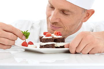 Image showing Baking, presentation and chef with cake for dessert isolated on a white background. Cooking, professional and man plating a sweet treat and fruit on a plate for fine dining service at a restaurant