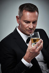 Image showing Man, tuxedo fashion and whiskey in studio isolated on a gray background. Alcohol, whisky and mature male model in stylish, designer and classy suit smelling aroma of alcoholic beverage in glass.