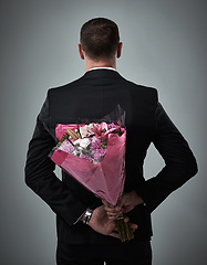 Image showing Valentines day, surprise bouquet and flowers of a man in a suit with love present behind back. Flower gift, suit and male model in a isolated gray background studio feeling romantic for a formal date