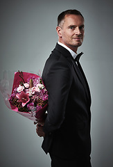 Image showing Surprise, portrait and man with flowers for a date isolated on a grey studio background. Classy, gift and mature person in a suit with a bouquet of roses as a present for valentines day on a backdrop