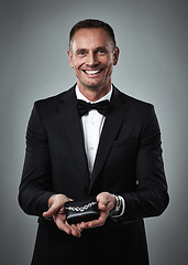 Image showing Jewelry, smile and portrait of a man giving a valentines present in a studio. Isolated, gray background and happy person in a suit with happiness holding a necklace gift feeling love and classy