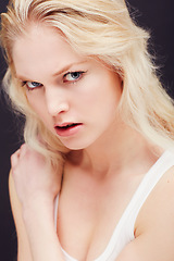 Image showing Portrait, beauty or fierce and a model woman in studio on a dark background frowning with confidence. Face, frown and skincare with an attractive young blonde female posing indoor for desire