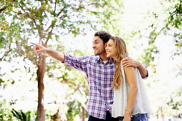 Image showing Couple, park and date of a woman and man together with love, care and hug in nature. Green trees, sunshine and happy people outdoor excited by pointing in the sun with happiness and good mood