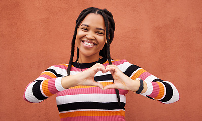 Image showing Heart shape, portrait and black woman by a wall in the city while on a walk on a vacation. Happy, smile and beautiful African female with love hand gesture in a town while on holiday or weekend trip.