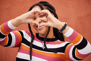 Image showing Happy, heart shape and black woman by a wall in the city while on a walk on a weekend trip. Happiness, portrait and African female with a love emoji or hand gesture in town on holiday or vacation.