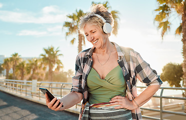 Image showing Happy, music and phone with old woman at beach for streaming, freedom and summer break. Internet, technology and headphones with senior lady listening to online radio for podcast, audio and media