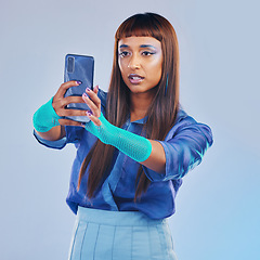 Image showing Fashion, selfie and woman with smartphone and cyberpunk neon clothing isolated on blue background. Social media, future and trendy gen z influencer from India with phone in studio for profile picture