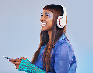Image showing Headphones, black woman and phone isolated on blue background for cyberpunk fashion and gen z thinking. Young person or beauty model with idea or listening to music on smartphone technology in studio