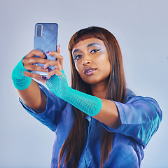 Image showing Fashion, selfie and woman with smartphone and cyberpunk neon clothing isolated on blue background. Social media, future and trendy gen z influencer from India with phone in studio for profile picture